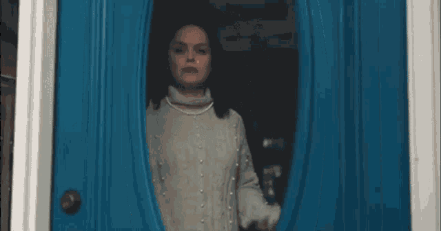 a woman is standing in front of a blue door looking out the window .