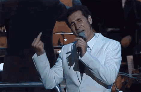 a man in a white suit singing into a microphone while giving the middle finger