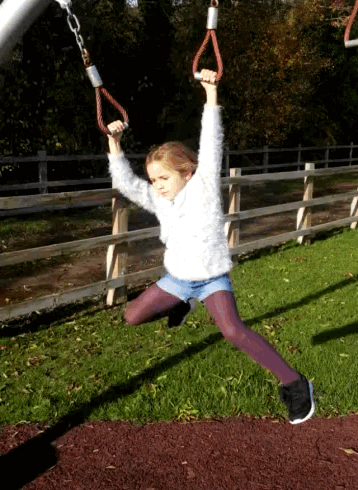 a young girl is swinging on a set of rings in a park