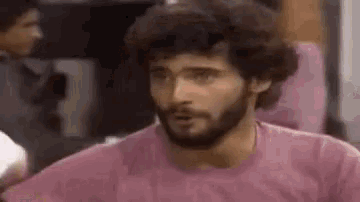 a man with a beard wearing a pink shirt is standing in a room .