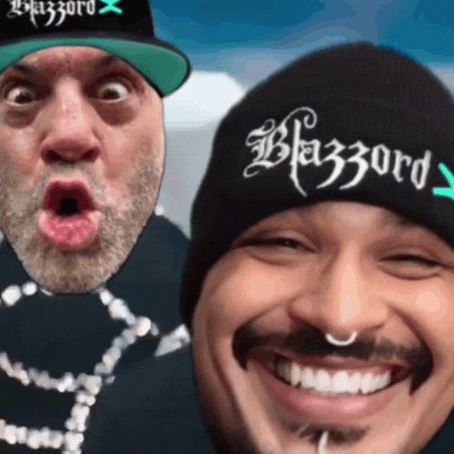 two men are posing for a picture and one has a beanie that says blazzard on it
