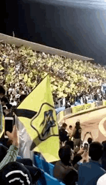 a crowd of people are watching a soccer game in a stadium with a yellow flag .