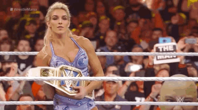 a woman is holding a wrestling championship belt in a ring