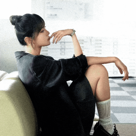 a woman sits on a couch with her hand on her chin