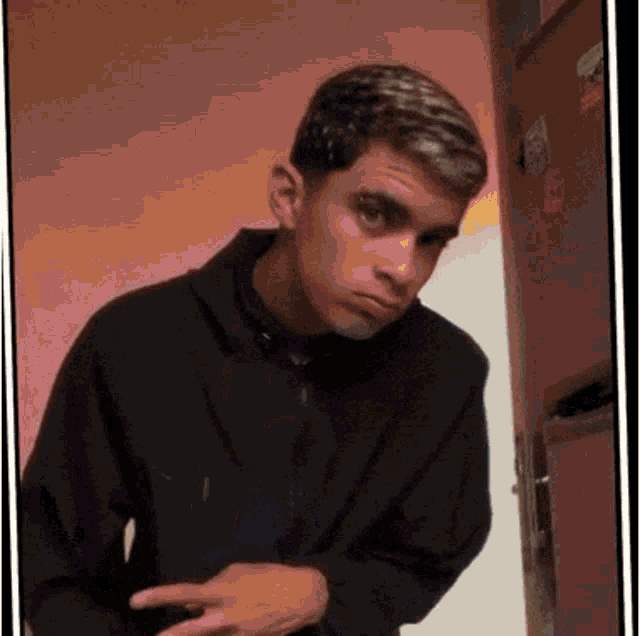 a young man in a black hoodie is standing in front of a refrigerator .