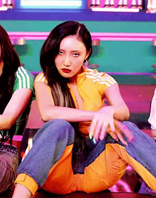 a woman in a yellow adidas shirt is sitting on the floor with her legs crossed and looking at the camera .