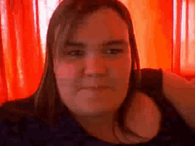 a woman with long hair is sitting in front of a red curtain .