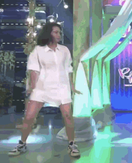 a woman wearing a white shirt and shorts is dancing on a stage