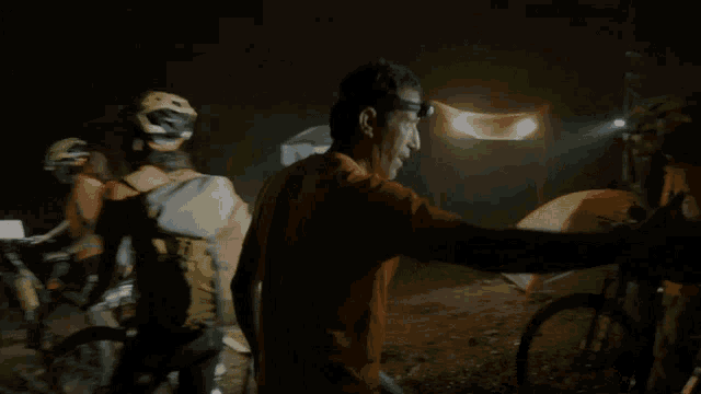 a man wearing a headlamp stands in front of a group of people on bikes