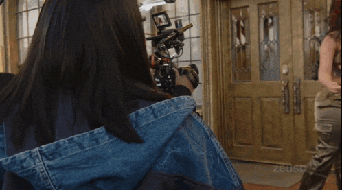 a woman in a denim jacket is being filmed by a camera with the word zeus on the bottom