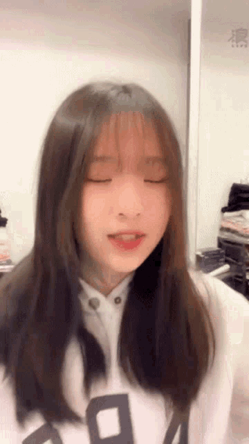 a girl with long hair and bangs is wearing a white sweatshirt with the letter a on it