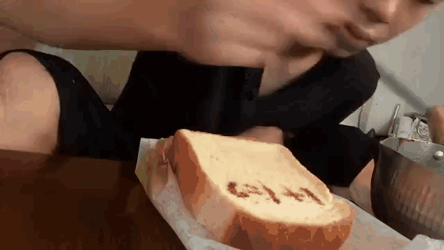 a person is sitting at a table eating a sandwich with the word gm written on it .
