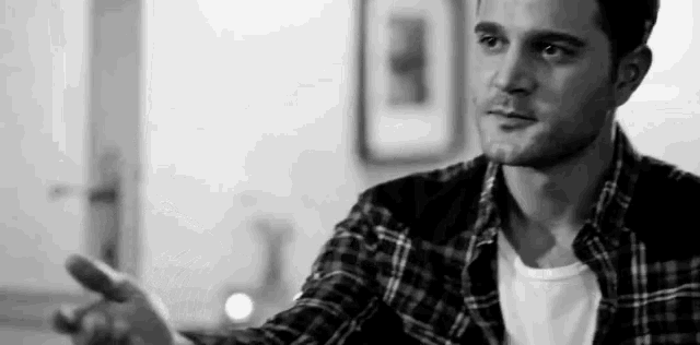 a black and white photo of a man in a plaid shirt talking to another man .