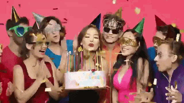 a woman blowing out candles on a birthday cake surrounded by people wearing party hats