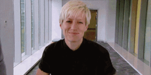 a woman with blonde hair is smiling in a hallway with a lot of windows .