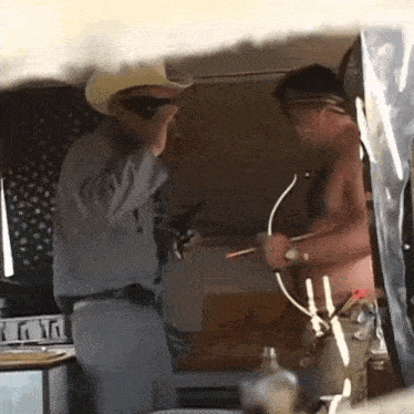 a man in a cowboy hat is holding a gun while another man holds a bow and arrow .