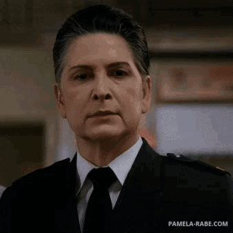 a woman in a black suit and tie is looking at the camera .