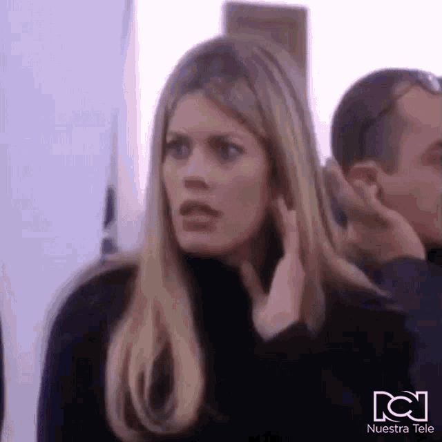 a woman is talking on a cell phone while standing next to a man and another woman .