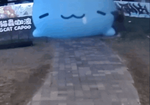 a person is walking down a brick walkway next to a large blue cat shaped object .