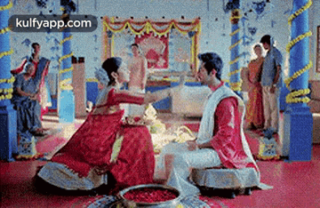 a bride and groom are sitting on the floor at a wedding ceremony in a room .
