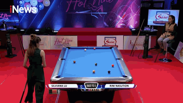 a woman stands in front of a pool table with a scoreboard that says race to 3