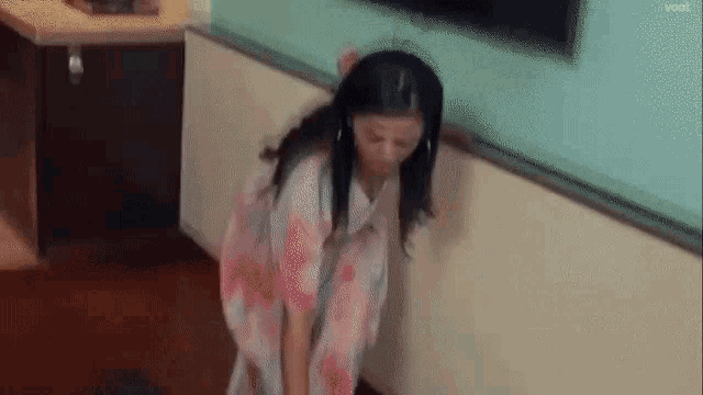 a woman in a pink and white dress is standing on a wooden floor next to a wall .