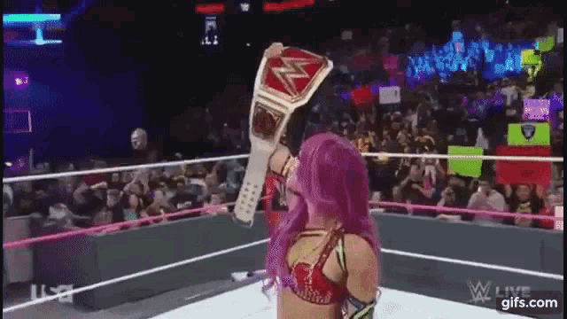 a woman with purple hair is standing in a wrestling ring holding a championship belt .