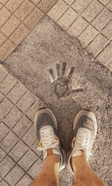 a person 's feet are standing in front of a hand print on the sidewalk