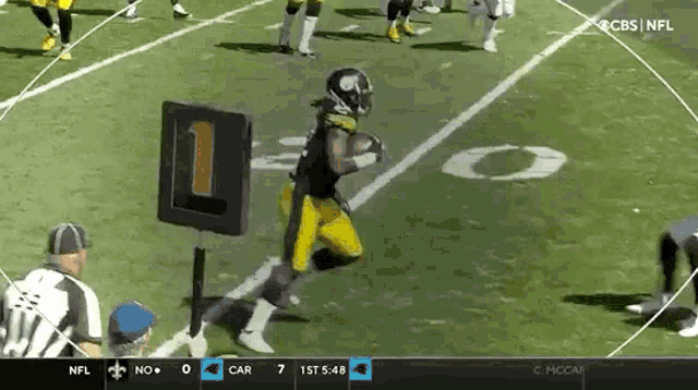 a football player is running with the ball on a field while a referee watches .