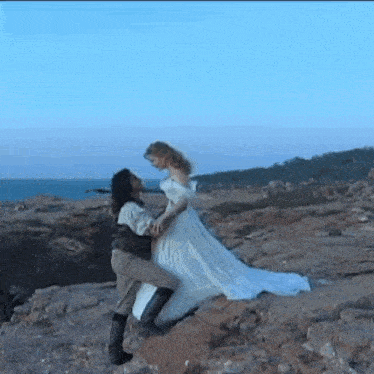 a man in a white dress is holding a woman in a white dress on top of a rocky hill .