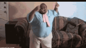 a man wearing a blue shirt and a pink tie is dancing on a couch .