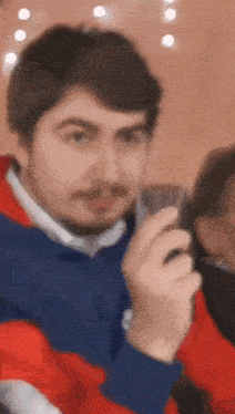 a man with a beard is holding a cell phone in his hand and looking at the camera .