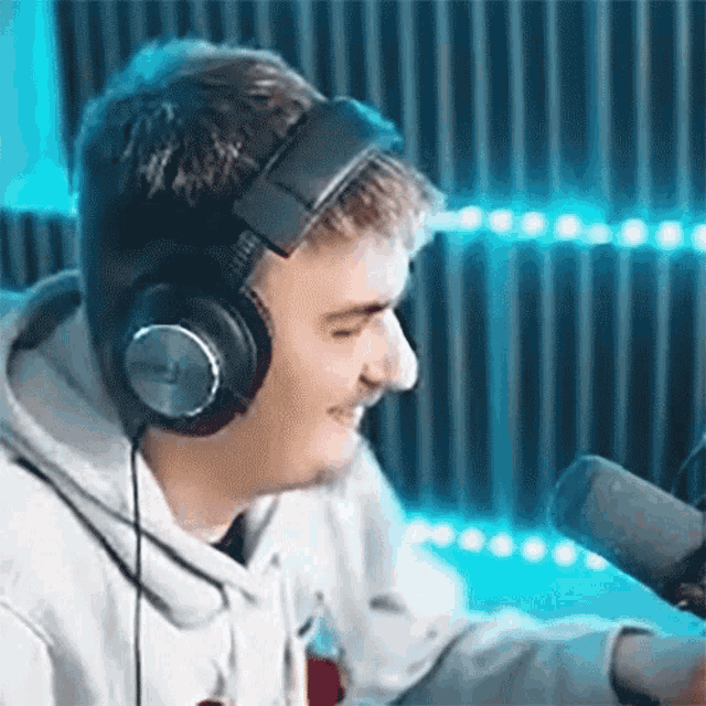 a man wearing headphones is smiling in front of a microphone in a studio .