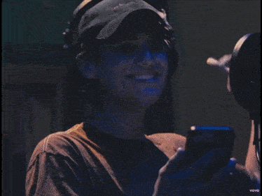 a man wearing headphones and a baseball cap is smiling and looking at his phone