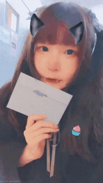 a girl with cat ears is holding a piece of paper in her hand