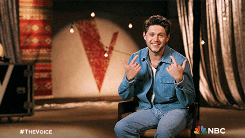 a man in a denim jacket is sitting in front of a curtain and giving the middle finger