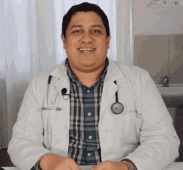 a doctor with a stethoscope around his neck is smiling and wearing a white coat