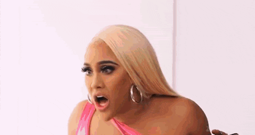 a woman in a pink top and hoop earrings is making a surprised face .