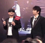 a man in a tuxedo stands next to another man in a white shirt