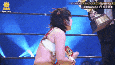 a woman in a wrestling ring is holding a trophy with #pw_mg on the bottom