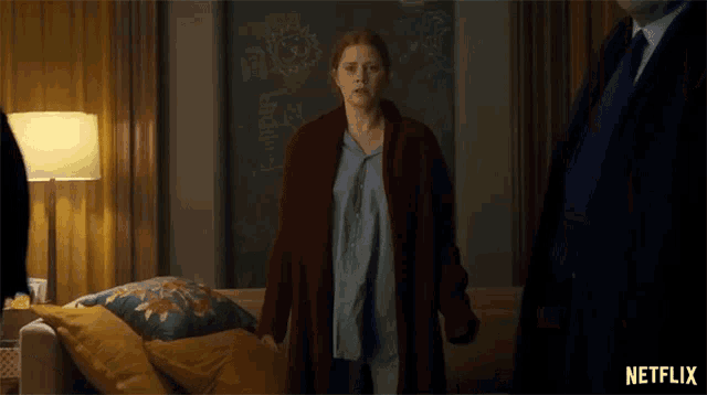 a woman in a red coat is standing in a living room next to a man in a suit and tie .