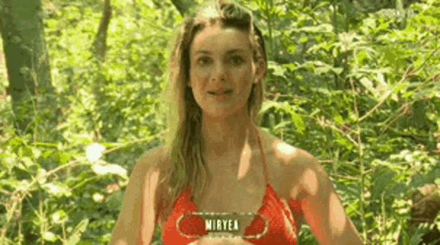 a woman in a red bikini is standing in the woods with a sign that says miryea