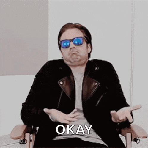 a man wearing sunglasses is sitting in a chair and saying okay
