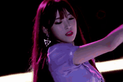 a woman with long red hair is wearing a purple dress and earrings and dancing on a stage .