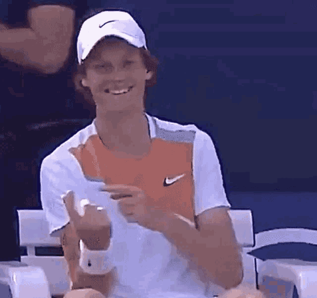 a man wearing a hat and a white shirt is smiling and pointing at something .