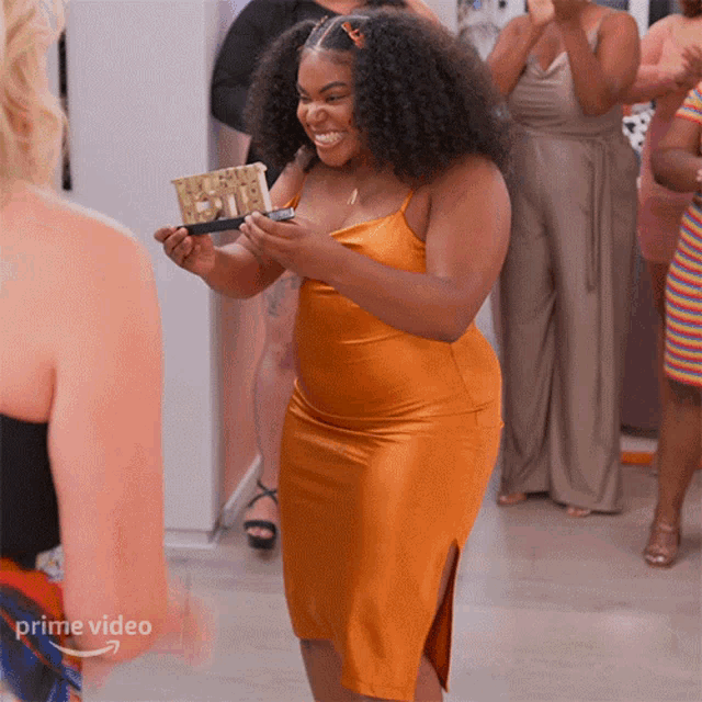 a woman in an orange dress is holding a trophy and smiling