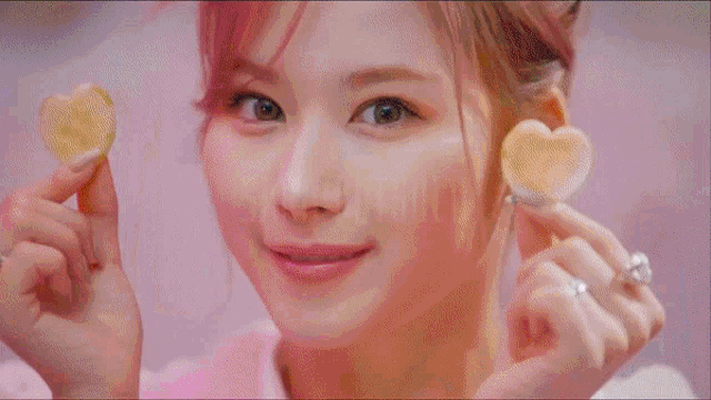a girl with pink hair is holding a heart shaped snack in front of a sign that says sara dutsoll