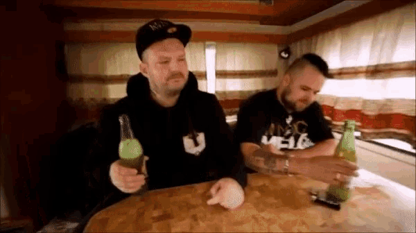 two men are sitting at a table holding beer bottles