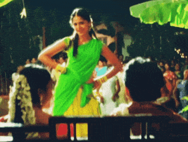 a woman in a green top and yellow skirt is standing in front of a crowd