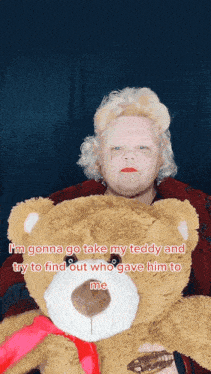 a woman is holding a teddy bear with a red ribbon around its neck